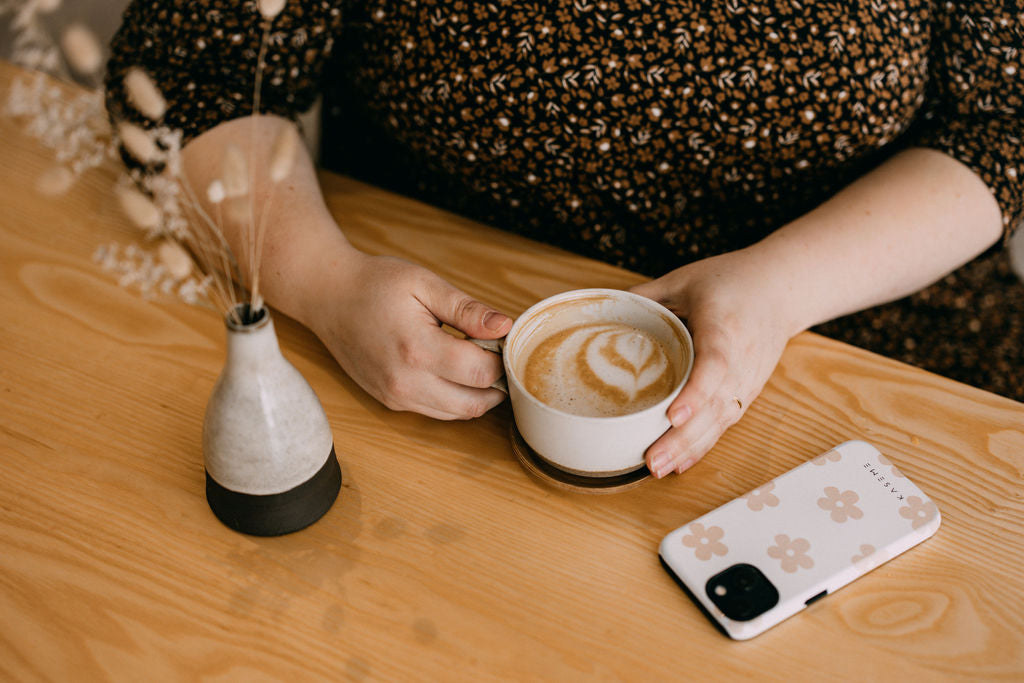 Heidi's holding a cup of coffee and her iphone is right next to her hand, along with a little vase.